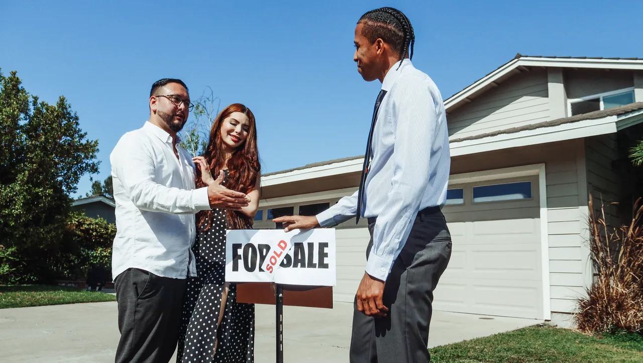 A real estate agent with a couple beside a sold sign